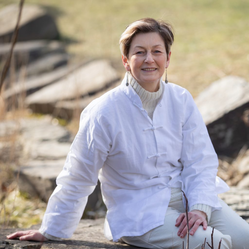 Zhineng Qigong Teacher smiling in white on a tree stump in nature